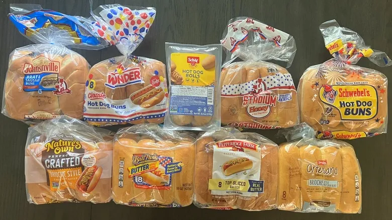 Top view of nine different brands of hot dog buns bagged and laid on a dark table