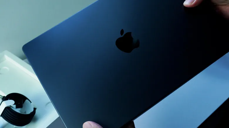 A closed blue 13-inch M5 Macbook Air being held on the sides by two hands