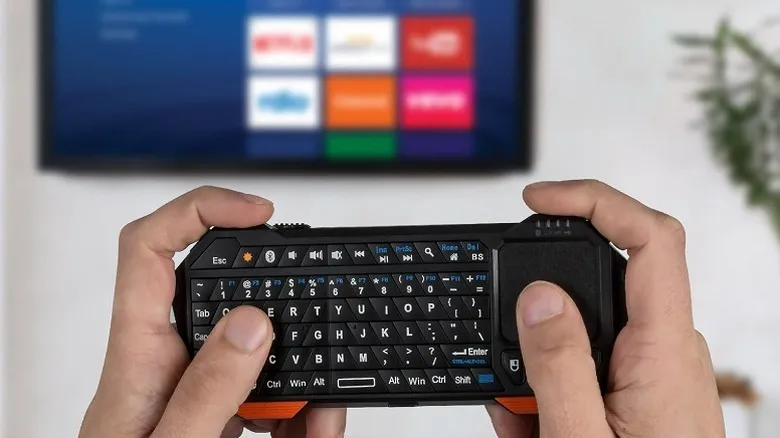 Typing on a mini keyboard connected to a smart TV on the wall.