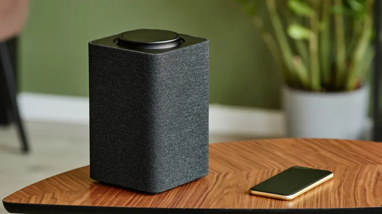 A portable speaker on a table next to a smartphone in a modern living room