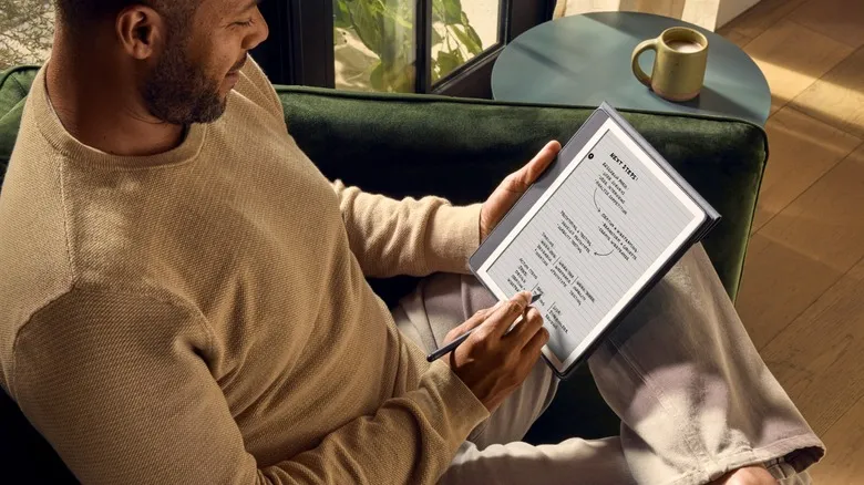 Person relaxing on seat while writing on an Amazon Kindle Scribe