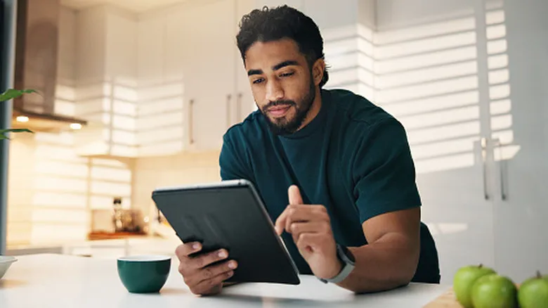Man using tablet at kitchen counter while browsing or reading content