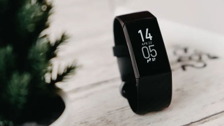 The Fitbit Charge 4 on a table beside a plant.