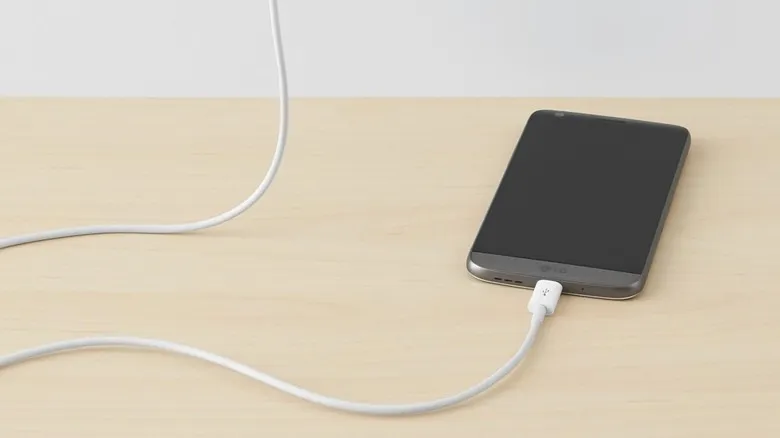 An Amazon Basics USB-C Fast Charger Cable connected to a cellphone on a light wooden countertop
