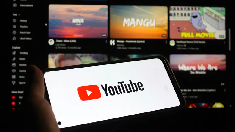 The YouTube logo on a smartphone with the website's interface on a screen in the background.