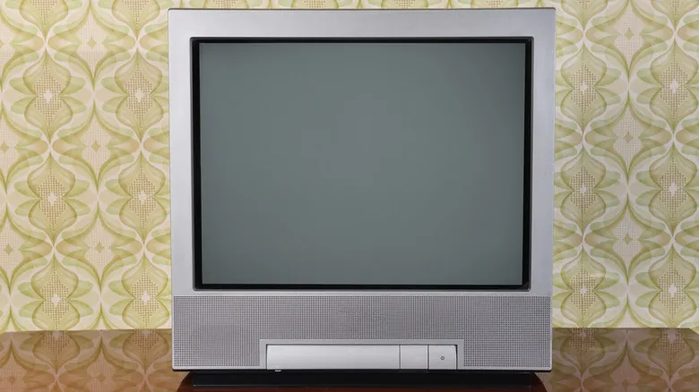 Flat-screen television with a blank screen on a wooden surface, set against retro patterned wallpaper.