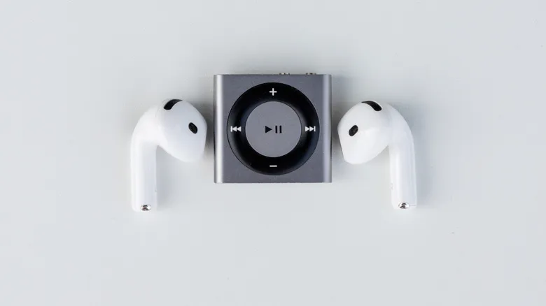 Compact MP3 player placed between two wireless earbuds on white background