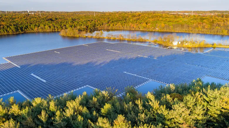 An aerial view shows a floating solar panel plant on a reservoir surrounded by lush forests.