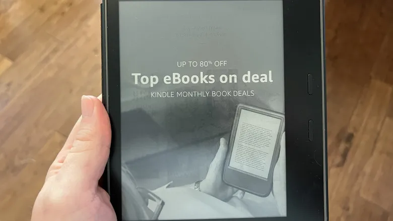 A hand holding an older Kindle eReader advertising a promotion with a wooden floor in the background