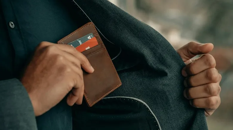 Man sliding RFID wallet with credit cards visible into jacket pocket.