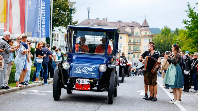 an old blue electric car driving down a festival street