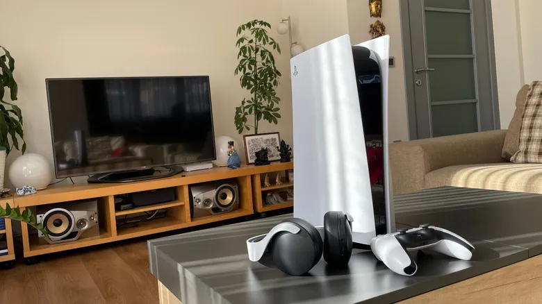 A PS5, a DualSense controller, and a Pulse wireless headset on a living room table in front of a media console.