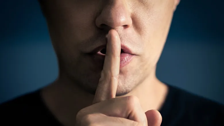 Person with fingers to their lips in a shushing motion to represent censorship