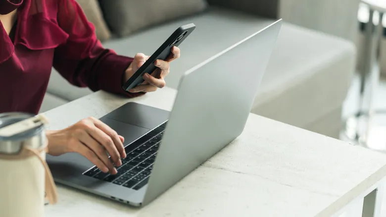 a person holding up a smartphone next to a laptop