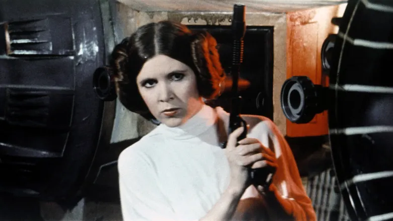 Carrie Fisher as Princess Leia holding a gun in Star Wars