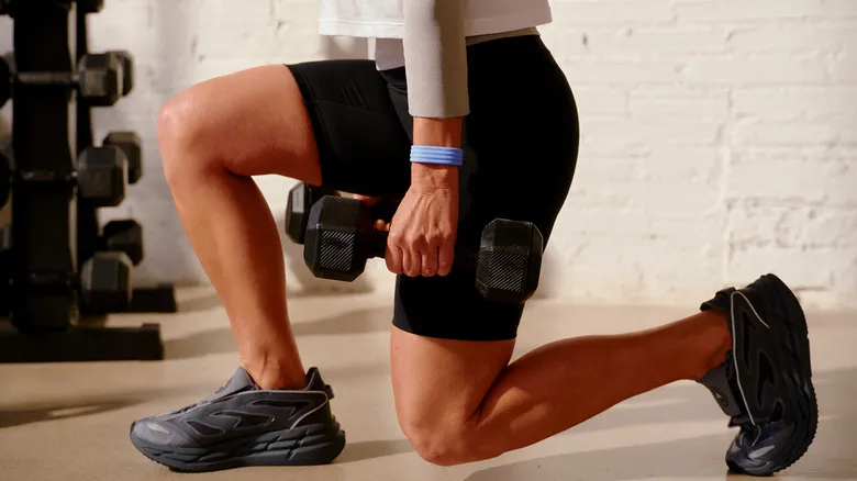 A woman lunging with weights while wearing the new Fitbit Air tracker.